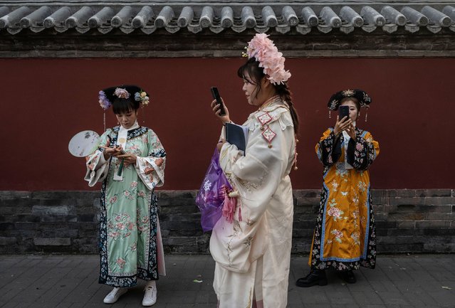 Women wearing traditional dress, known as Hanfu, look at their mobile phones as they visit a historic neighbourhood during the Golden Week holiday on October 3, 2024 in Beijing, China. China marked its National Day and the 75th anniversary of the founding of the Peoples Republic on October 1st. (Photo by Kevin Frayer/Getty Images)