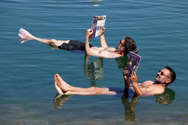This handout picture released by the Amman International Film Festival (AIFF) shows Lebanese actor Georges Khabbaz (R) and Amman International Film Festival jury member Phil Jandaly (back) reading the festivals programme as they float in the Dead Sea on July 25, 2022. (Photo by Patrick Baz/Amman International Film Festival (AIFF)/AFP Photo)