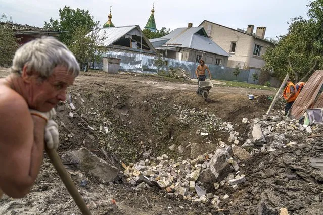 Workers clear debris next to a crater caused by a rocket strike on a house in Kramatorsk, Donetsk region, eastern Ukraine, Friday, August 12, 2022. There were no injuries reported in the strike. (Photo by David Goldman/AP Photo)