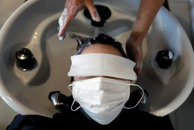 Customer Natsuki Suda, wearing a protective mask to prevent infection, receives hair treatment from the owner of hair salon Pinch, Akihiro Yoshida, following the coronavirus disease (COVID-19) outbreak, in Tokyo, Japan, April 28, 2020. According to Yoshida, the revenue of his salon in April falls less than 50 percent of the usual season and now it accepts one customer at a time by appointment only as a measurement for preventing the infection. (Photo by Kim Kyung-Hoon/Reuters)