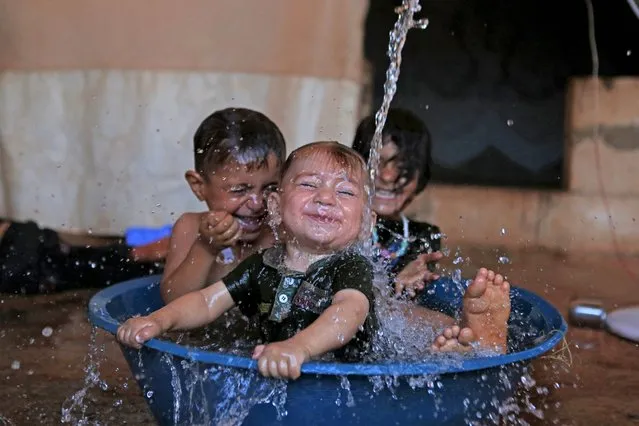 Children play in a makeshift pool in the back of a pick-up truck amid soaring temperatures, in a camp for the internally displaced near the Syrian village of Killi in the rebel-held northwestern province of Idlib, on July 31, 2022. (Photo by Aaref Watad/AFP Photo)