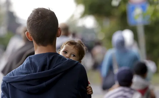 A migrant holds a child as he walks down a street from Keleti train station in Budapest, Hungary, September 5, 2015. (Photo by David W. Cerny/Reuters)