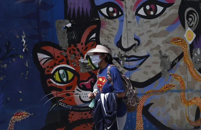 A woman wearing a face mask as a precaution against the new coronavirus walks past a mural in La Paz, Bolivia, Tuesday, April 21, 2020. Bolivia's government is restricting residents to essential shopping in the mornings, in an attempt to contain the spread of the new coronavirus. (Photo by Juan Karita/AP Photo)