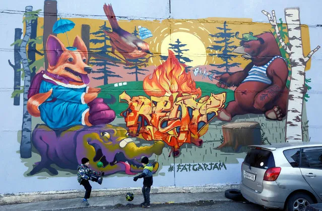 Сhildren play with balls near a wall of a district heating hub with the graffiti artwork “Forest Camp” created by Alexei Lazarev, a member of an artists' team, during a graffiti festival in Krasnoyarsk, Siberia, Russia October 9, 2017. (Photo by Ilya Naymushin/Reuters)