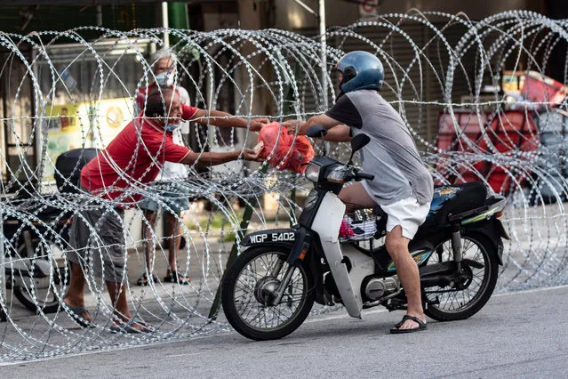 A resident receives food supply from a motorist through a barb wire in Petaling Jaya outside Kuala Lumpur, Malaysia, 12 May 2020. The area was locked down after 15 people were diagnosed with Covid-19. Business resumed after more than 40 days. (Photo by Ahmad Yusni/EPA/EFE)