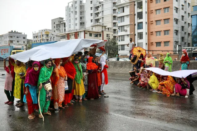 Garments workers take shelter under a banner as it starts to rain, as they block a road demanding their due wages during the lockdown amid concerns over the coronavirus disease (COVID-19) outbreak in Dhaka, Bangladesh, April 15, 2020. (Photo by Mohammad Ponir Hossain/Reuters)