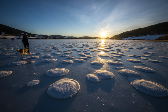 Strollers walk between pancakes snow on the frozen Lake des Rousses in Les Rousses, central-eastern France, on January 1, 2025. This phenomenon forms when slushy ice in water clumps into round, pancake-like shapes due to waves or currents. (Photo by Fabrice Coffrini/AFP Photo)