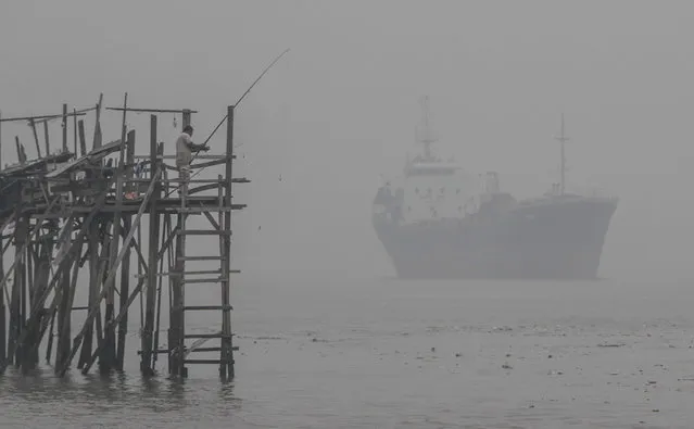 A man fishes against an anchored tanker shrouded with haze in Port Klang, outside Kuala Lumpur, Malaysia on Sunday, September 13, 2015. Wildfires caused by illegal land clearing in Indonesia's Sumatra and Borneo islands often spread choking haze to neighboring countries such as Malaysia and Singapore. (Photo by Joshua Paul/AP Photo)