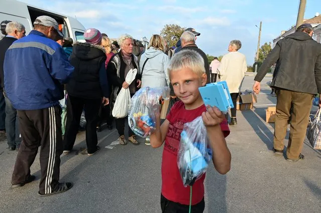 A young boy holds bags of humanitarian aid from a christian religious organization distributed to local residents in Izyum, Kharkiv region, on September 28, 2022, amid the Russian invasion of Ukraine. (Photo by Sergey Bobok/AFP Photo)
