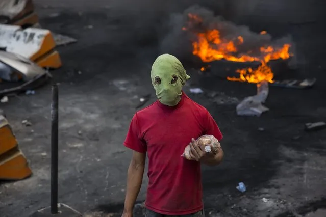 A masked supporter of presidential candidate Salvador Nasralla carries cookies at a burning roadblock where demonstrators protest what they call electoral fraud in Tegucigalpa, Honduras, Friday, December 1, 2017. As the wait for Sunday's election results has dragged on, rock-wielding protesters have increasingly taken to the streets against riot police armed with tear gas, batons and water cannons. (Photo by Rodrigo Abd/AP Photo)