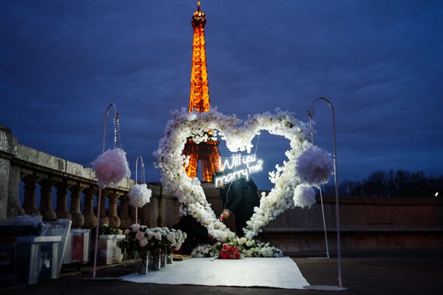 A woman prepares a heart of flowers with the words “Will you marry me” while the Eiffel Tower is seen in the background, on the eve of the annual celebrations of Valentine's Day in Paris, on February 13, 2024. (Photo by Dimitar Dilkoff/AFP Photo)
