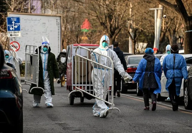 Health workers wearing personal protective equipment (PPE) carry barricades inside a residential community that just opened after a lockdown due to Covid-19 coronavirus restrictions in Beijing on December 9, 2022. (Photo by Noel Celis/AFP Photo)
