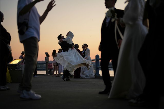 A couple wearing wedding outfits dance during a photo session at the Galata Bridge in Istanbul, Turkey, Friday, June 13, 2025. (Photo by Francisco Seco/AP Photo)