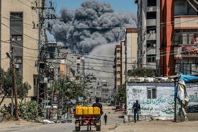 A cloud of smoke erupts down the road from an explosion as a man drives an animal-drawn cart loaded with jerrycans in Nuseirat in the central Gaza Strip on April 17, 2024 amid the ongoing battles in the Palestinian territory between Israel and the militant group Hamas. (Photo by AFP Photo/Stringer)
