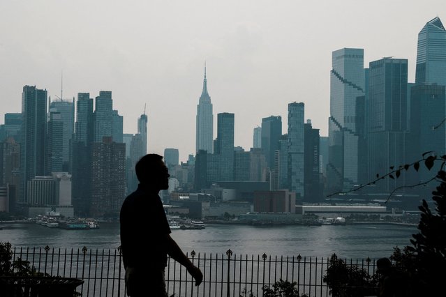 A person walks at a local park, while haze and smoke caused by wildfires in Canada linger over the skyline of midtown Manhattan as seen from Weehawken, New Jersey, on August 5, 2025. (Photo by Eduardo Munoz/Reuters)