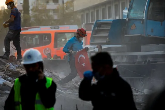 A worker holds a national flag as rescue operations take place on a site after an earthquake struck the Aegean Sea, in the coastal province of Izmir, Turkey, November 2, 2020. (Photo by Kemal Aslan/Reuters)