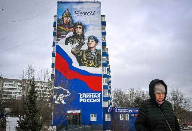 A pedestrian walks near a residential building which houses the local branch of Russia's ruling party, United Russia, with its emblem bear and a patriotic mural on the wall in the town of Chekhov, some 75 kilometres outside Moscow, on February 11, 2023. Despite strict government censorship and the threat of jail, residents of Russia's capital are finding subtle ways to express alarm and dissent over the Kremlin's year-long offensive in Ukraine. The messages are barely visible but omnipresent throughout Moscow, scrawled and graffitied on walls, pasted as stickers on drain pipes or carved into the wood of benches. (Photo by Yuri Kadobnov/AFP Photo)