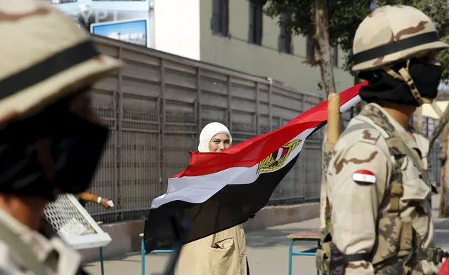 A woman waves an Egyptian national flag near soldiers standing guard outside a school used as a polling station during the second round of parliament elections at Heliopolis in Cairo, Egypt, November 22, 2015. Egyptians voted on Sunday in the second phase of elections that are meant to restore parliament after a more than three-year hiatus but which critics say have been undermined by widespread repression. (Photo by Amr Abdallah Dalsh/Reuters)