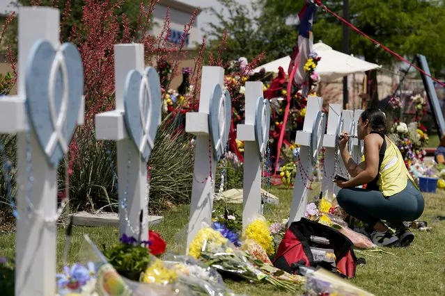 A woman signs a cross that stands by others at a makeshift memorial for the victims of a mass shooting, Monday, May 8, 2023, in Allen, Texas. (Photo by Tony Gutierrez/AP Photo)
