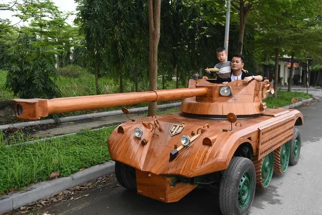 Truong Van Dao and his son ride in a wooden tank made from the conversion of an old minibus in a residential area in Bac Ninh province on March 28, 2022. A Vietnamese father spent hundreds of hours, investing thousands, to convert an old van into a wooden tank for his son – an unusual hobby in a country once ravaged by war. (Photo by Nhac Nguyen/AFP Photo)