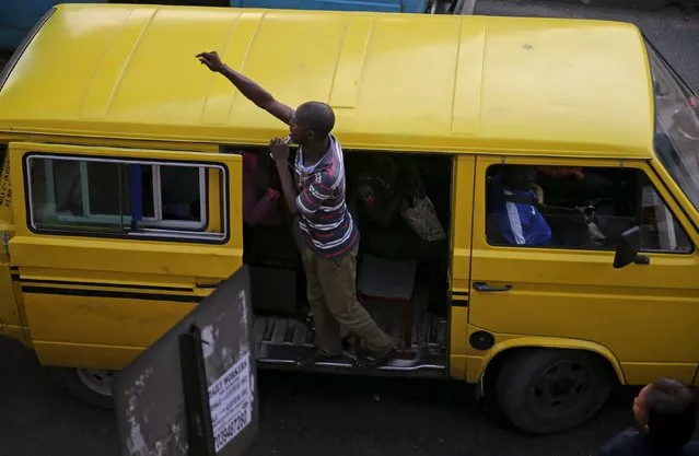 A bus conductor hangs out of a bus as he calls for passengers at the Obalende area, in Nigeria's commercial capital Lagos November 23, 2015. (Photo by Akintunde Akinleye/Reuters)