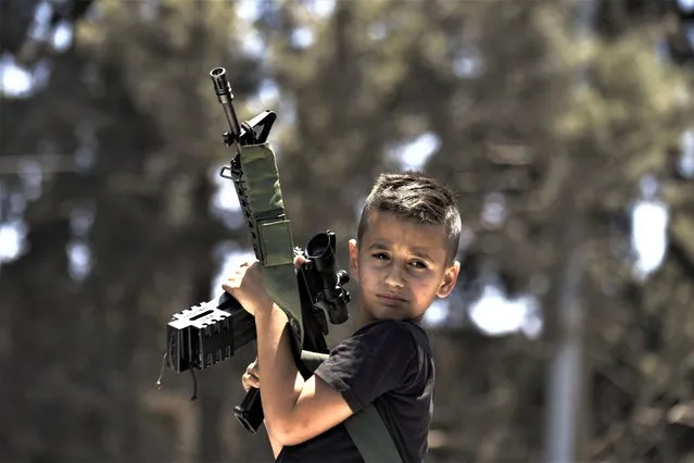 A Palestinian kid holds an M-16 rifle during the funeral of those who were killed during an Israeli army operation, in the Jenin refugee camp, West Bank, Wednesday, July 5, 2023. The Israeli military says it withdrew its troops from the camp on Wednesday, ending an intense two-day operation that killed at least 13 Palestinians, drove thousands of people from their homes and left a wide swath of damage in its wake. One Israeli soldier was also killed. (Photo by Majdi Mohammed/AP Photo)