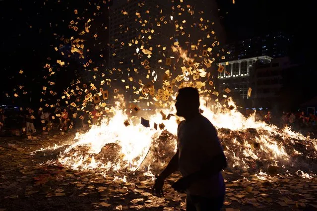 Ethnic Chinese throw paper offerings during burning of a giant paper statue of the Chinese deity “Da Shi Ye” or “Guardian God of Ghosts” during the Chinese Hungry Ghost Festival in Kuala Lumpur, Malaysia, late Thursday, August 31, 2023. The Hungry Ghost Festival is celebrated during the seventh month of the Chinese lunar calendar, when prayers are offered to the dead and offerings of food and paper-made models of items such as televisions, refrigerators and sport cars are burnt to appease the wandering spirits. It is believed that the gates of hell are opened during the month and the dead ancestors return to visit their relatives. (Photo by Vincent Thian/AP Photo)