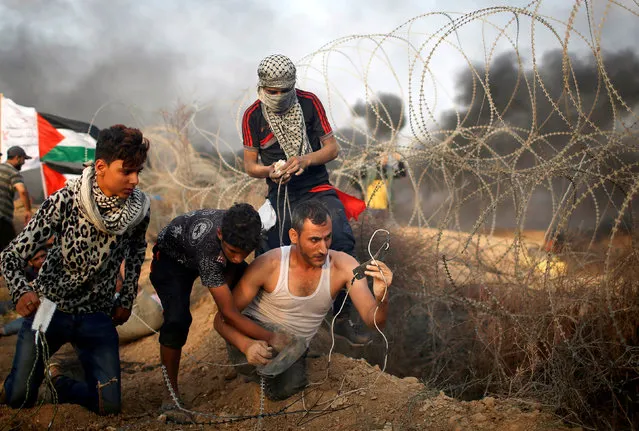 A disabled Palestinian is helped as he uses a sling to hurl stones at Israeli troops during a protest calling for lifting the Israeli blockade on Gaza and demanding the right to return to their homeland, at the Israel-Gaza border fence in Gaza October 19, 2018. (Photo by Mohammed Salem/Reuters)