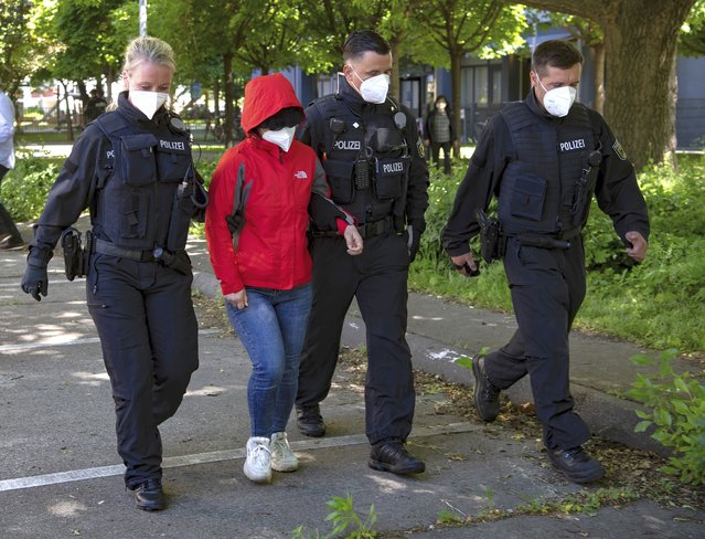 Police officers lead a woman to a vehicle during a raid against a group of people suspect to brought Vietnamese people to Europe on fraudulently obtained visas, in Berlin, Germany, May 31, 2021. Authorities say suspects have been arrested in Germany and Slovakia in raids on a group accused of smuggling Vietnamese people into Germany and other European countries for large fees that they had to work off in massage parlors and brothels among other places. (Photo by Paul Zinken/dpa via AP Photo)