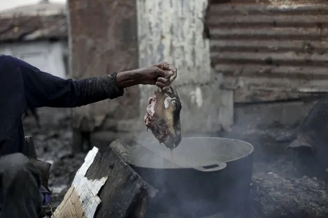 Jesner Sakage takes a goat head out of a pot at La Saline slaughterhouse in Port-au-Prince, Haiti, March 20, 2015. (Photo by Andres Martinez Casares/Reuters)