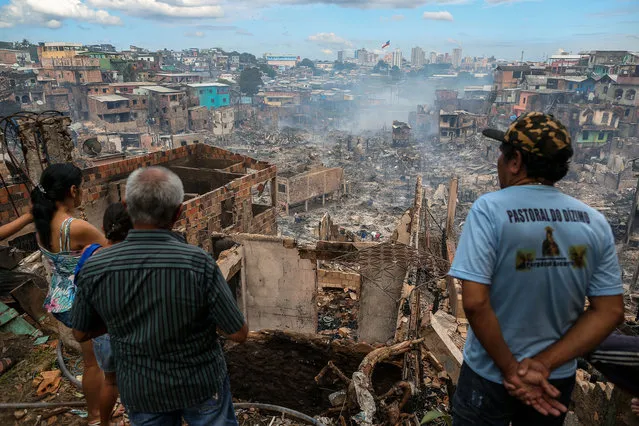 Residents look at the remains of Educandos neighbourhood the day after it was ravaged by a massive fire, in Manaus, Amazonas state, Brazil on December 18, 2018. A huge fire blazed through 600 wooden homes built on stilts next to a river in Brazil's Amazon region overnight, decimating a poor area of the city of Manaus but causing no deaths. An initial investigation suggests a pressure cooker on a stove started the fire, which rapidly spread, fanned by strong gusts of wind at the time, authorities said. (Photo by Michael Dantas/AFP Photo)