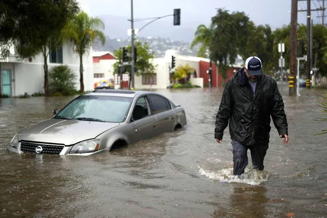 A man walks past a submerged vehicle on a flooded street, Thursday, December 21, 2023, in Santa Barbara, Calif. (Photo by Jae C. Hong/AP Photo)