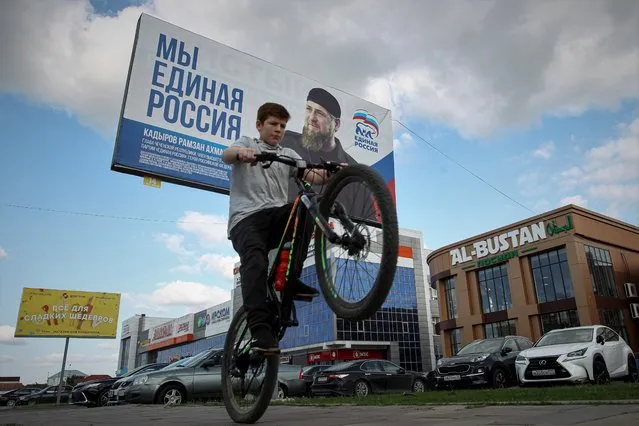 A boy rides his bicycle in a street with an election poster of United Russia party with a portrait of Chechnya's regional leader Ramzan Kadyrov ahead of the parliamentary election to the State Duma, the Lower House of the Russian Parliament and local parliament in Grozny, Russia, Tuesday, September 14, 2021. The Parliamentary elections will be held in Russia on Sunday, Sept. 19. (Photo by Musa Sadulayev/AP Photo)