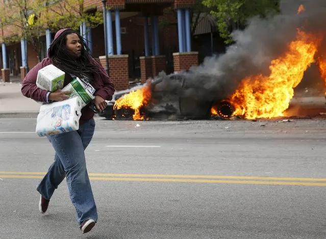 A woman with goods looted from a store runs past burning vehicles during clashes in Baltimore, Maryland April 27, 2015. Seven Baltimore police officers were injured on Monday as rioters threw bricks and stones and burned patrol cars in violent protests after the funeral of Freddie Gray, a black man who died in police custody. (Photo by Shannon Stapleton/Reuters)