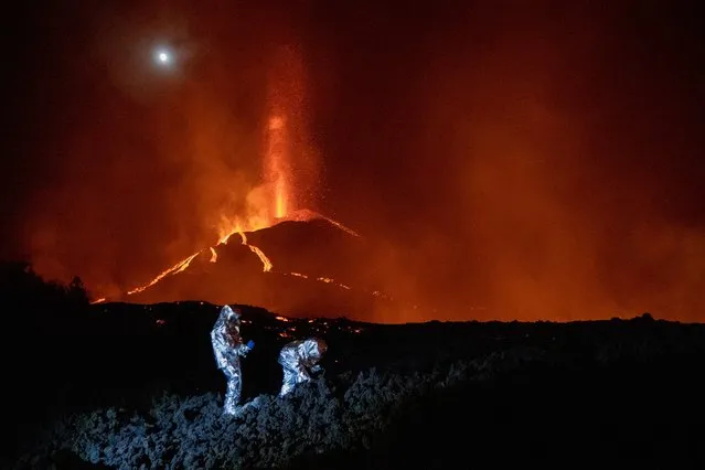 In this handout photograph taken and released by the Spanish Military Emergency Unit (UME) on October 16, 2021, members of the GIETMA (Technological and Environmental Emergencies Intervention Group) of the UME monitor the evolution of a new lava flow, following the eruption of the Cumbre Vieja volcano, on the Canary island of La Palma. There is no prospect of the volcanic eruption in Spain's Canary Islands ending “in the short or medium term”, experts said on October 13, 2021 after three-and-a-half weeks of activity. (Photo by Luismi Ortiz/UME/AFP Photo)
