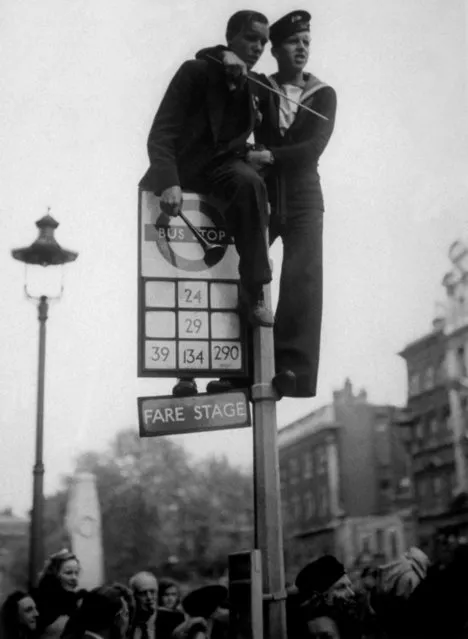 8th May 1945: A sailor and a civilian clamber on top of a bus stop in Whitehall, London, during the VE Day celebrations. (Photo by Keystone/Getty Images)