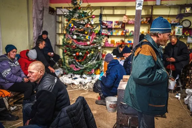 Local residents gather close to a Christmas tree as they rest inside a humanitarian aid centre in Bakhmut, Donetsk region, on January 6, 2023, as the Russia-Ukraine war enters its 316th day. Like every other day this week, holdout residents of this all-but-destroyed city on Ukraine's front line flocked to a ground-floor humanitarian aid centre on January 6, 2023, desperate for food and internet access. And like every other day this week, shelling rained down around Bakhmut into the afternoon, giving the lie to President Vladimir Putin's demand that Russian troops observe a 36-hour ceasefire which, had it been respected, would have begun before midday. As they sipped hot tea and slurped noodles around a woodstove, the crowd of mostly elderly civilians said they were not surprised fighting had continued in a city that lies in ruins after months of fierce combat, the worst of the 10-month war. (Photo by Dimitar Dilkoff/AFP Photo)