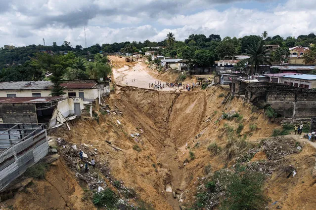 Residents gather on the edge of the landslide left by the collapse of one of the main roads in the Mont Ngafula district in Kinshasa, the capital of the Democratic Republic of Congo on November 4, 2021. Every year, during the rainy season, pieces of roads, houses, schools, shops, and administrative buildings are blown away by the collapse of sections of hillsides. Anarchic urbanisation and lack of road maintenance lead to loss of life and the destruction of infrastructures. (Photo by Alexis Huguet/AFP Photo)