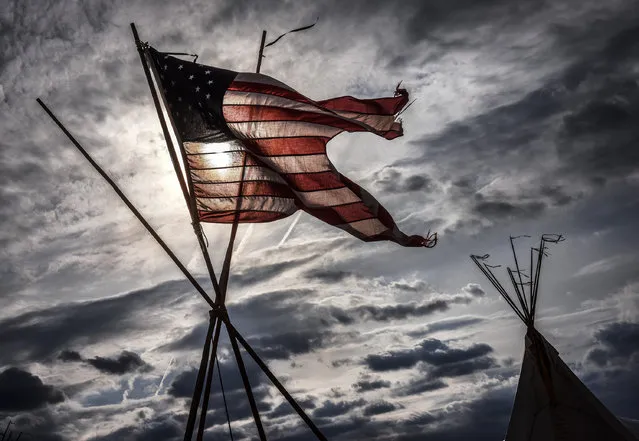 Sunlight shines through a well worn US flag as Native American tipi's are erected on the Monument grounds in advance of a march by Standing Rock members against the pipeline on March, 07, 2017 in Washington, DC. (Photo by Bill O'Leary/The Washington Post)