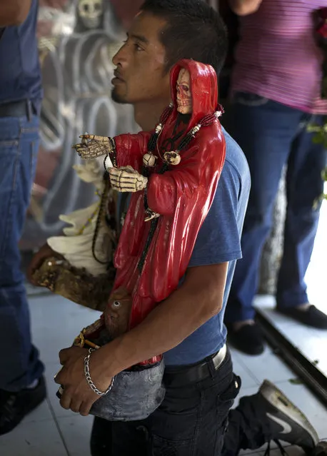 In this March 1, 2017 photo, a devotee of the Death Saint or “Santa Muerte” holds his statue of the folk saint inside Mercy Church on the edge of Mexico City's Tepito neighborhood. After asking for a favor, offerings are shared among the followers; tacos, pastries, apples, sodas and amulets are passed from hand to hand. Alcohol is sprayed and cigarette smoke blown over the Death Saint repeatedly. (Photo by Marco Ugarte/AP Photo)