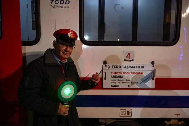 A train conductor poses next to a sign of the Eastern Express train before the departure at Erzurum train station on January 6, 2022. Festive garlands, red tablecloths and enticing bottles pop out the moment passengers clamber aboard the Eastern Express train before it glides off on an epic voyage across Turkey's snow-capped plateaus along the Euphrates. Called Dogu Ekspresi in Turkish, the train offers one of the expansive country's most coveted new experiences. (Photo by Ozan Kose/AFP Photo)