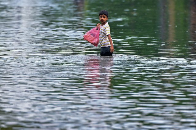 A boy wades through a flooded street after heavy rains in Malwana on the outskirts of Colombo on May 27, 2024. (Photo by Ishara S. Kodikara/AFP Photo)