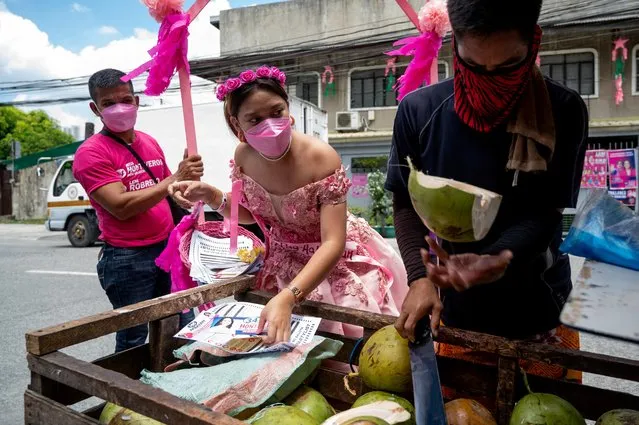 A woman wearing a gown hands out campaign leaflets to a coconut juice vendor during a Santacruzan-themed house-to-house campaign for Philippine Vice President and presidential candidate Leni Robredo, in Quezon City, Metro Manila, Philippines, May 5, 2022. (Photo by Lisa Marie David/Reuters)