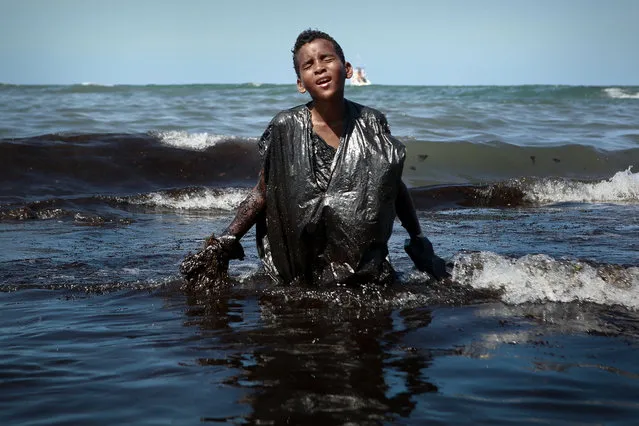 A boy walks out of the sea while removing oil spilled on Itapuama beach located in the city of Cabo de Santo Agostinho, Pernambuco state, Brazil, on October 21, 2019. Large blobs of oil staining more than 130 beaches in northeastern Brazil began appearing in early September and have now turned up along a 2,000km stretch of the Atlantic coastline. The source of the patches remain a mystery despite President Jair Bolsonaro's assertions they came from outside the country and were possibly the work of criminals. (Photo by Leo Malafaia/AFP Photo)