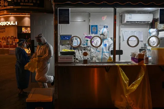 Health workers are seen in a cabin where swab samples are taken in the Jing' an district of Shanghai on June 12, 2022. (Photo by Hector Retamal/AFP Photo)