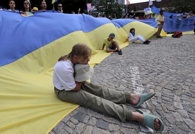 A girl sits on a huge Ukrainian flag during a demonstration against the war in Ukraine in Garmisch-Partenkirchen, Germany, on Sunday, June 26, 2022. The Group of Seven leading economic powers are meeting in Germany for their annual gathering Sunday through Tuesday. (Photo by Alexandra Beier/AP Photo)