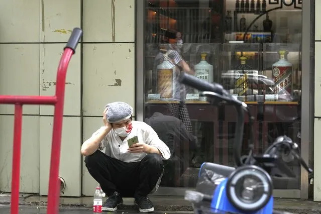 A restaurant cook wearing a mask takes a break out on the sidewalk, Monday, June 27, 2022, in Beijing. (Photo by Ng Han Guan/AP Photo)