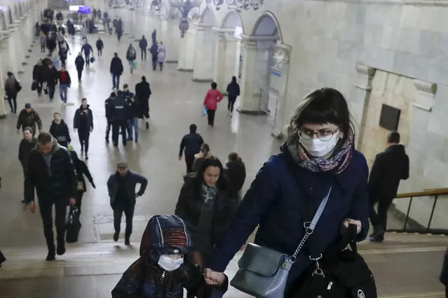 A woman with her child wear medical masks walk inside the Komsomolskaya Metro (subway) station in Moscow, Russia, Wednesday, March 18, 2020. Authorities in Russia are taking vast measures to prevent the spread of the disease in the country. The measures include closing the border for all foreigners, shutting down schools for three weeks, sweeping testing and urging people to stay home. (Photo by Pavel Golovkin/AP Photo)