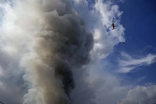 A helicopter extinguishes a fire at a warehouse of the online retailer Ozon in Istra Municipal District, northwest Moscow Region, Russia, Wednesday, August 3, 2022. (Photo by Alexander Zemlianichenko/AP Photo)