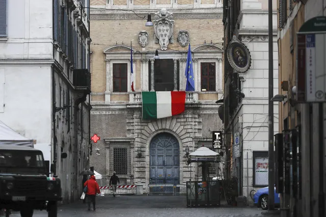 The Italian flag hangs from the balcony of the French Embassy in Rome, Friday, March 27, 2020. As the coronavirus claims lives, ruins livelihoods and wreaks economic havoc, tensions are rising between European Union countries over how best to respond as the pandemic overwhelms some member nations, once more raising troubling questions about the EU's ability to stand united in times of crisis. (Photo by Alessandra Tarantino/AP Photo)